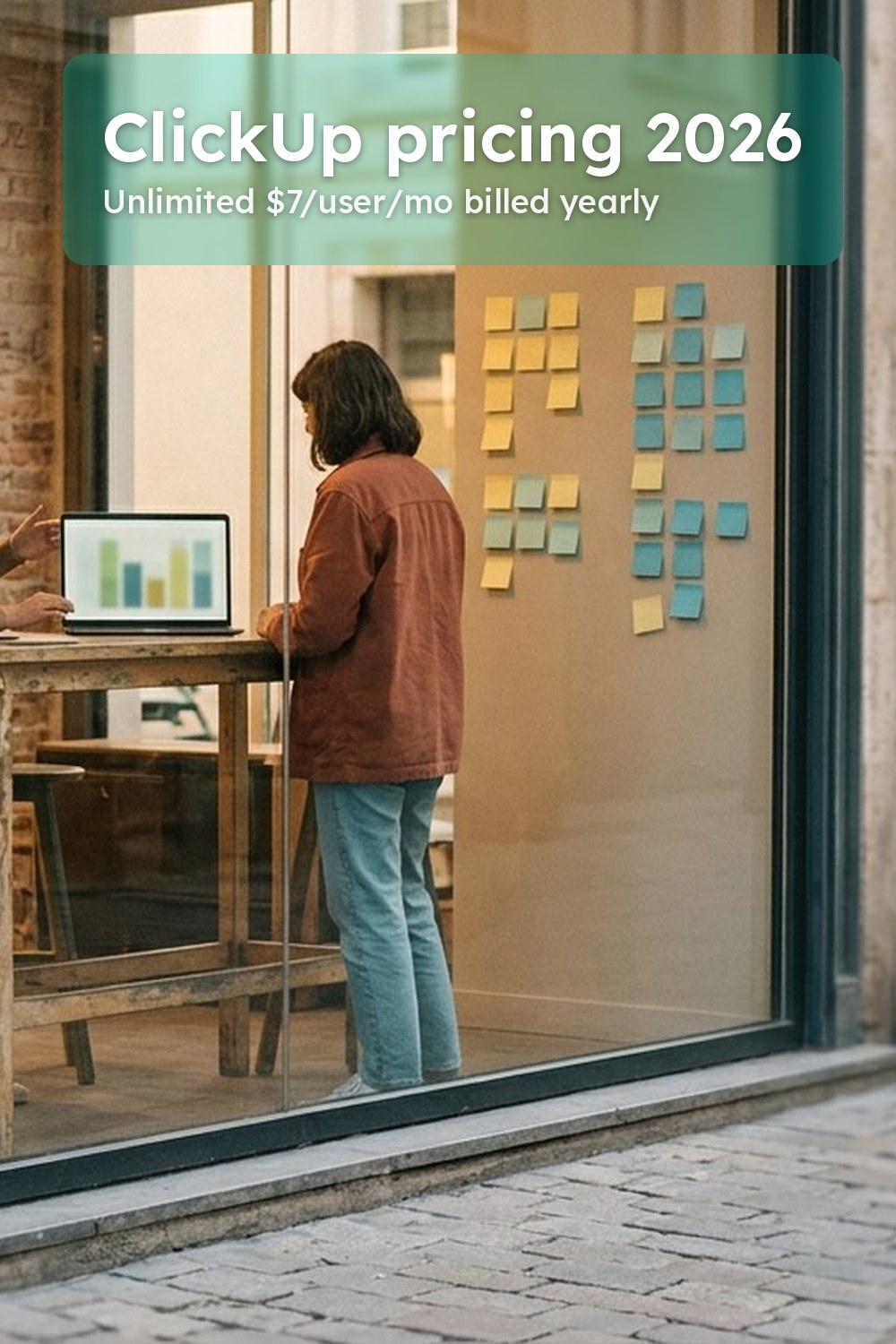 Three people seen from behind around a high table with a laptop and a wall of sticky notes in a co-working space, a scene
